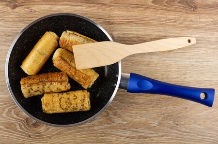Frying pan with fried pancake rolls, spatula on wooden table. Top view