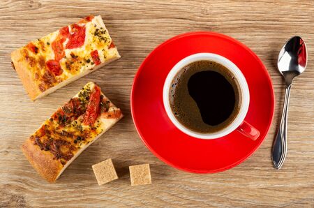 Pieces of khachapuri with tomato and basil, sugar cubes, cup with coffee on red saucer, spoon on wooden table. Top viewの写真素材
