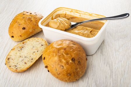 Buns, pieces of bread, plastic container with peanut butter and spoon on light wooden table