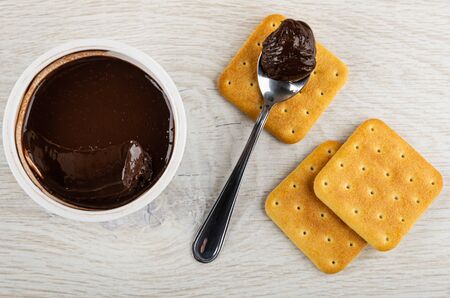 Plastic jar with chocolate melted cheese, crackers, teaspoon with chocolate cheese on wooden table....