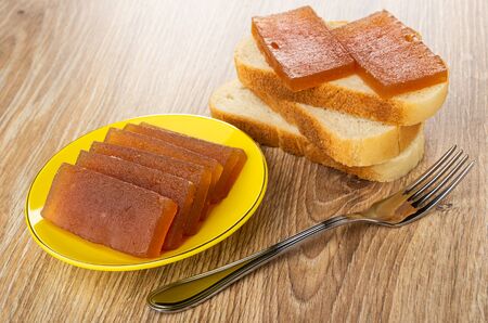 Sandwich with apple marmalade on pieces of wheat bread, yellow saucer with marmalade, fork on wooden...