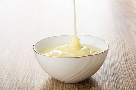 Pouring condensed milk in white glass bowl on wooden tableの写真素材