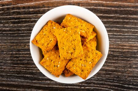 Crackers with tomato, sesame and oregano in white bowl on dark wooden table. Top viewの写真素材