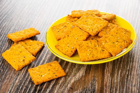 Crackers with tomato, sesame and oregano in yellow saucer, cookies on dark wooden tableの写真素材