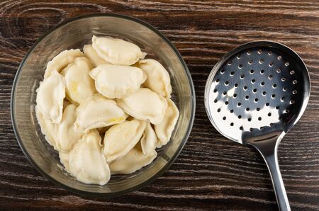 Boiled dumplings with butter in transparent bowl, skimmer on dark wooden table. Top viewの写真素材