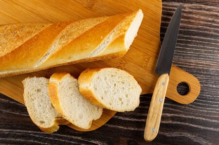 Loaf of wheat bread, slices of bread, kitchen knife on bamboo cutting board on dark wooden table....