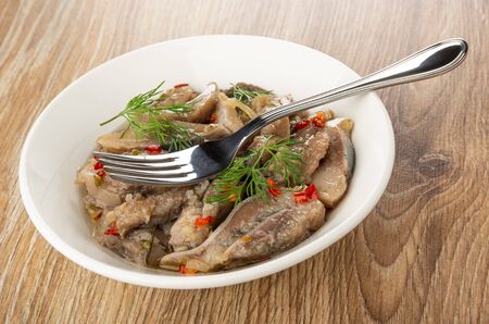 Fork on white plate with salted herring in vegetable oil on wooden table