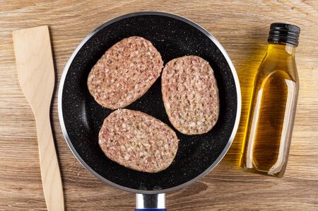 Spatula, raw pork cutlets in frying pan, bottle of vegetable oil on wooden table.の写真素材