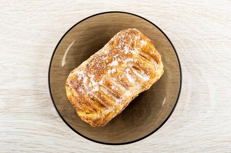 Puff in sugar powder on brown glass saucer on wooden table. Top view