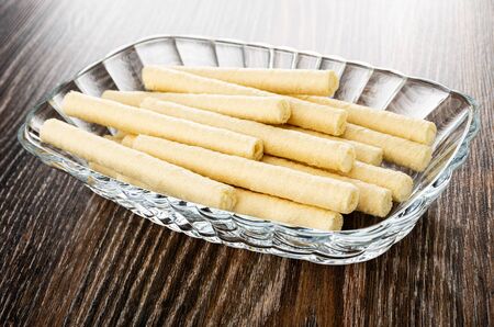 Heap of wafer rolls with filling in transparent glass bowl on dark wooden table