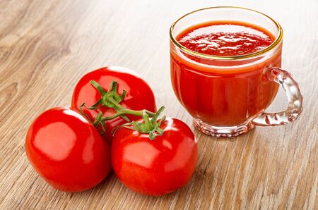 Red fresh tomatoes on branch, transparent cup of tomato juice on wooden tableの写真素材