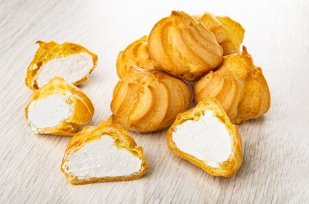 Few whole profiteroles and halves of  profiteroles on wooden table