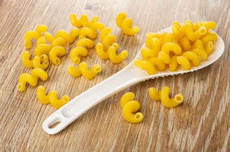 Scattered spiral pasta in white plastic spoon, on brown wooden tableの写真素材