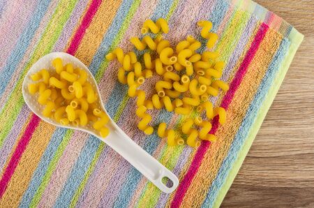 Scattered spiral pasta, pasta in white plastic spoon on striped napkin on wooden table. Top viewの写真素材