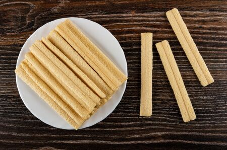 Heap of breadsticks with filling in white glass plate, few bread sticks on dark wooden table. Top...
