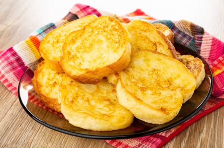 Dairy fried toasts in brown glass plate on checkered napkin on wooden table. Top view