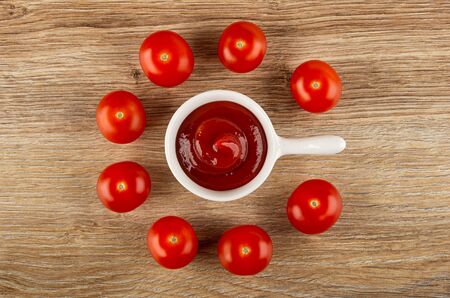 Few tomato cherry and ketchup in small sauceboat with handle on wooden table. Top viewの写真素材
