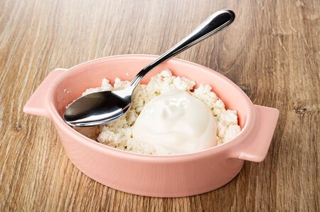 Spoon in pink glass bowl with defatted grained cottage cheese and sour cream on wooden tableの写真素材