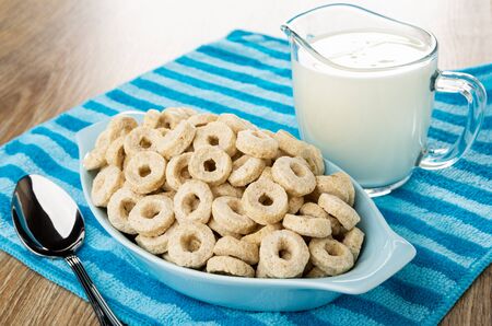 Blue glass bowl with corn rings, spoon, transparent pitcher with yogurt on striped napkin on wooden tableの写真素材