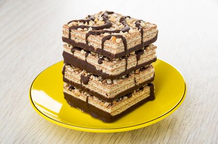 Stack of wafers with chocolate and peanut in yellow glass plate on wooden tableの写真素材