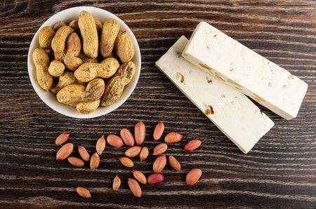 Goober in white bowl, peeled groundnut and nougat with peanut on dark wooden table. Top view