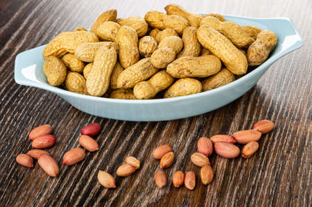 Groundnuts in blue glass bowl, scattered peanut on dark wooden table