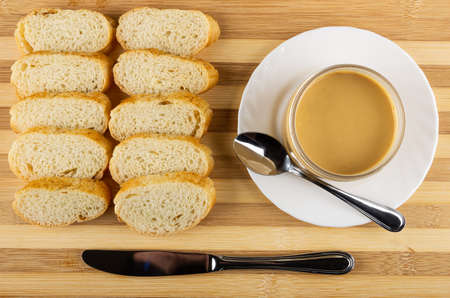 Row slices of wheat bread, jar with peanut butter, teaspoon in white plate, table knife on striped...