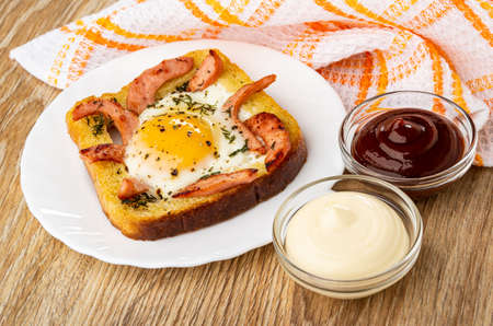 Checkered napkin, wheat bread sandwich with fried egg and sausages in white plate, bowls with...