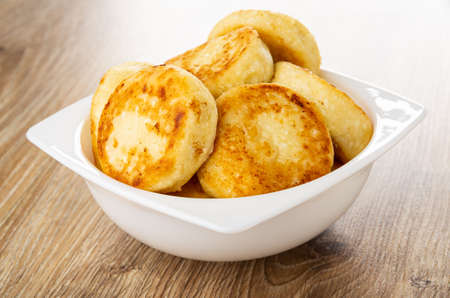 Heap of homemade small cottage cheese pancakes in white glass bowl on wooden table