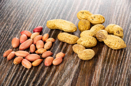 Scattered groundnuts and peeled peanut on dark wooden table