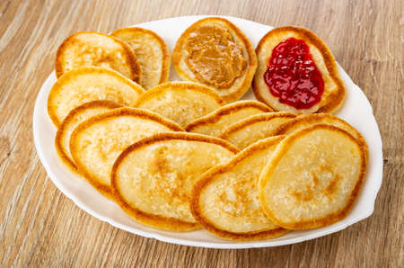 Pancakes with jam and peanut butter in dish on wooden table
