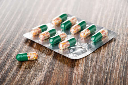 Blister of medicine in transparent capsules, single capsule on dark wooden table