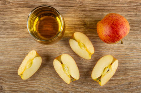 Glass with apple juice, pieces of apple and whole apple on brown wooden table. Top view