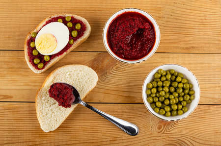Sandwich with beetroot caviar, green peas and egg, teaspoon on piece of bread, glass bowls with...