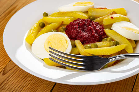 Fork in white plate with fried potato, green peas and beetroot caviar on wooden table