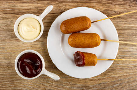 Sauce boats with mayonnaise and ketchup, fried sausages on bamboo skewers in white plate on wooden table. Top viewの写真素材
