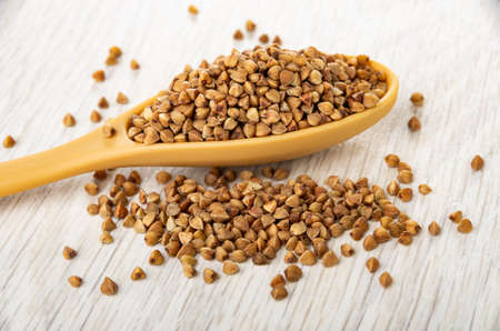 Scattered buckwheat, plastic spoon with raw buckwheat on wooden table