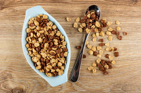 Cereal grains breakfast with chocolate and caramel in blue glass bowl, metallic spoon with cereal on...