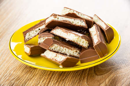 Heap of chocolate with dairy porous filling in yellow glass saucer on wooden table
