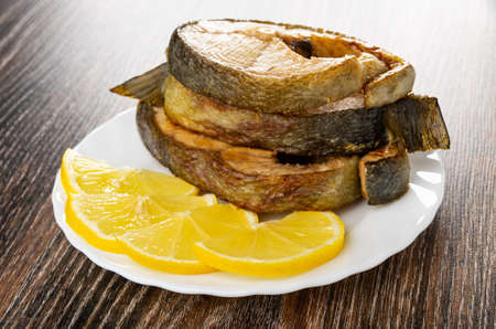 Few fried steak from salmon and slices of lemon in white plate on dark wooden table