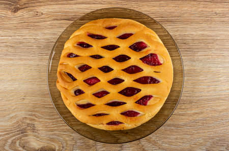 Round sweet wicker pie with raspberry jam in brown plate on wooden table. Top viewの写真素材