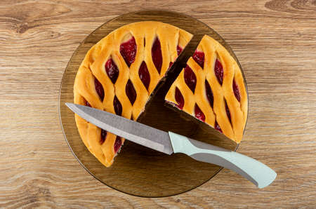 Pieces of wicker pie with raspberry jam in brown plate, kitchen knife on wooden table. Top viewの写真素材