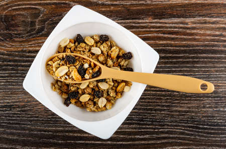 Plastic spoon in white bowl with cereal breakfast with peanut and raisin on dark wooden table. Top viewの写真素材