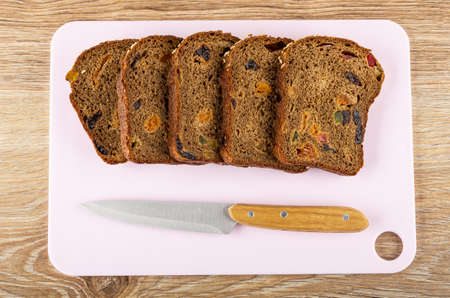 Row of slices of bread with fruits and seed, kitchen knife on pink cutting board on wooden table....