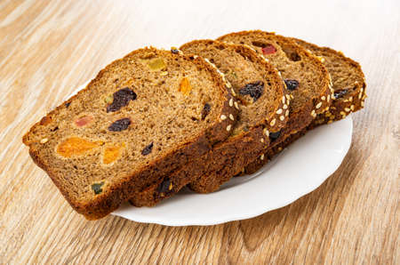 Slices of bread with fruits and seed in white plate on wooden table