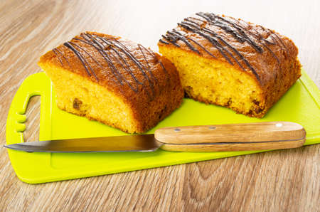 Two pieces of biscuit with raisin, kitchen knife on green cutting board on brown wooden table