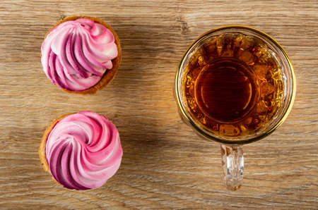 Two tartlets with pink buttercream, cup of tea on brown wooden table. Top viewの写真素材