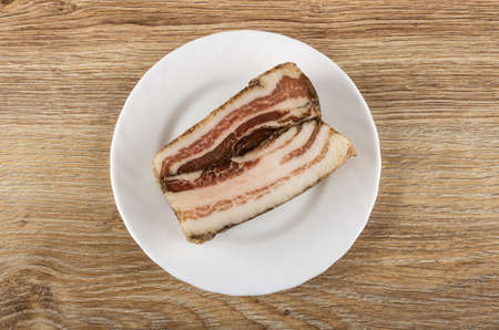 Piece of salted pork lard in white glass plate on wooden table. Top viewの写真素材