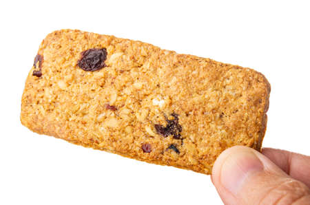 Single muesli cookie with cranberry in male fingers isolated on white background