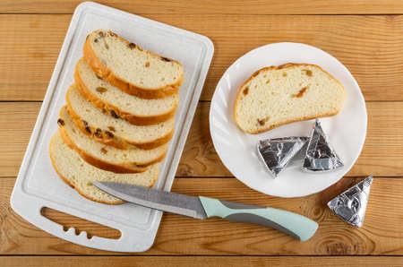 Slices of bread with raisin on cutting board, kitchen knife, slice of bread and slices of creamy...